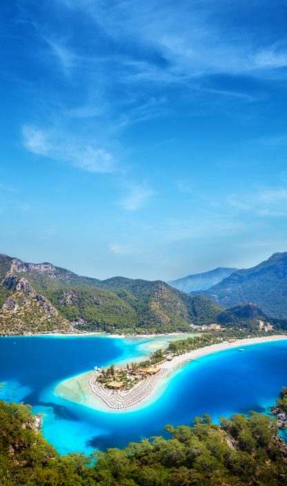 Aerial view of sea bay, sandy beach with umbrellas, trees, mount
